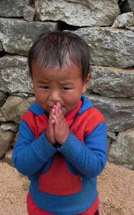 A young boy with his hands folded in front of a stone wall.