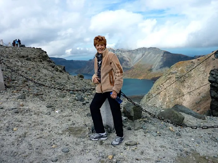 A woman standing on top of a mountain near a lake.