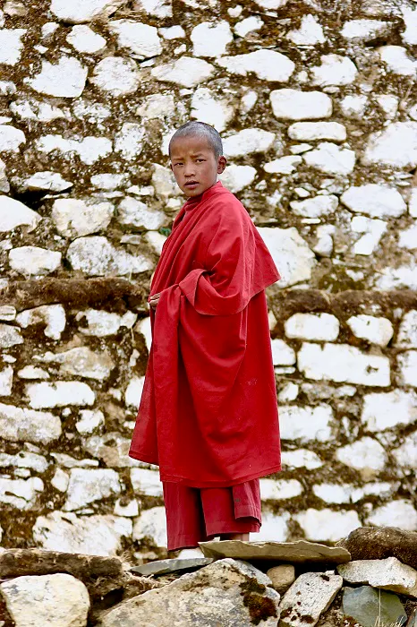 A young monk in a red robe standing on a stone wall.