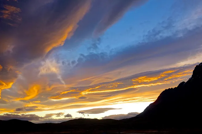 A sunset over a mountain with clouds in the sky.
