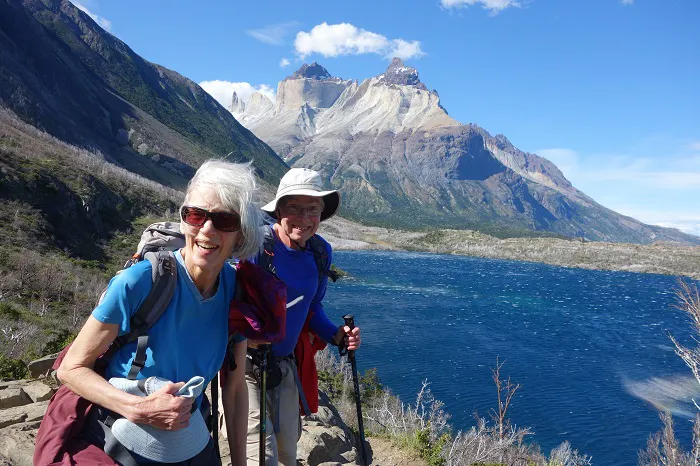 Two hikers on a trail with mountains in the background.