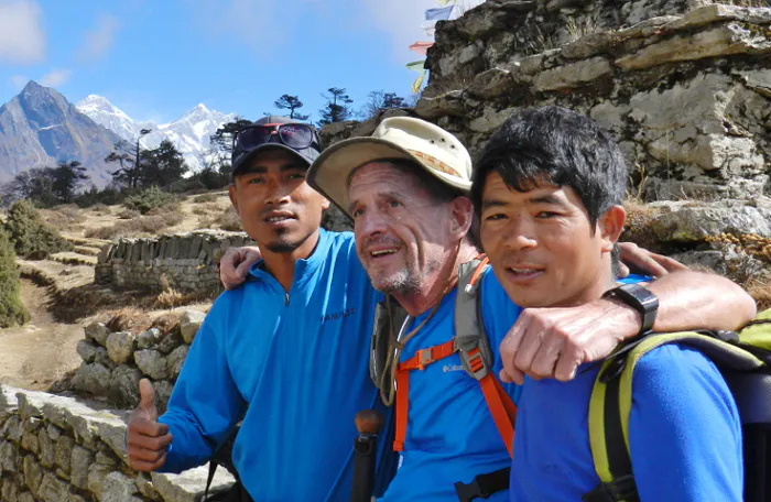 Three men standing on a hill with mountains in the background.