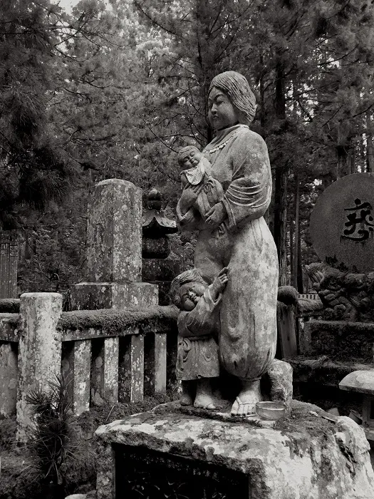 A black and white photo of a statue in a cemetery.