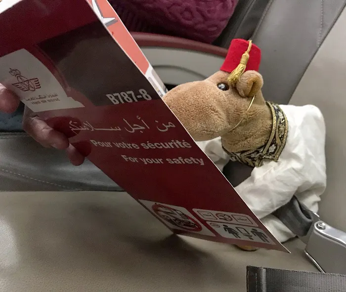 A stuffed camel is sitting in the seat of an airplane.