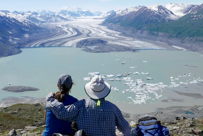 Two people looking at a glacier from the top of a mountain.
