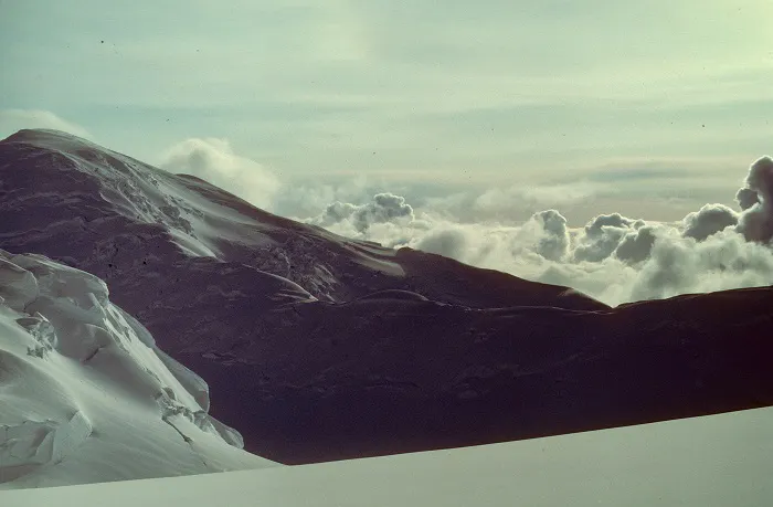 A snow covered mountain with clouds in the sky.