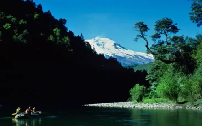 A group of people are rafting down a river with a mountain in the background.