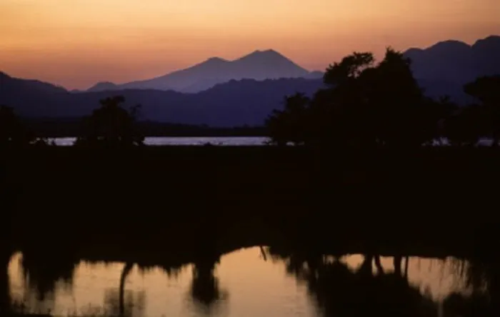The sun is setting over a lake with mountains in the background.