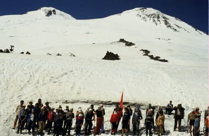 A group of people standing in front of a snow covered mountain.