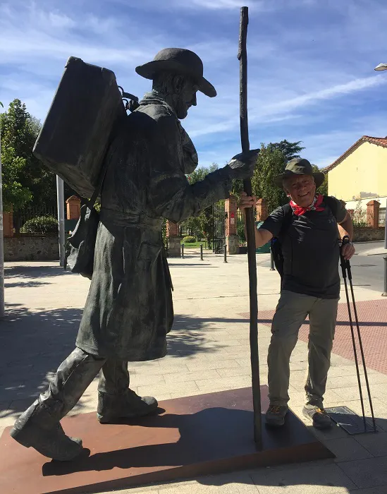 A man standing next to a statue of a man with a backpack.