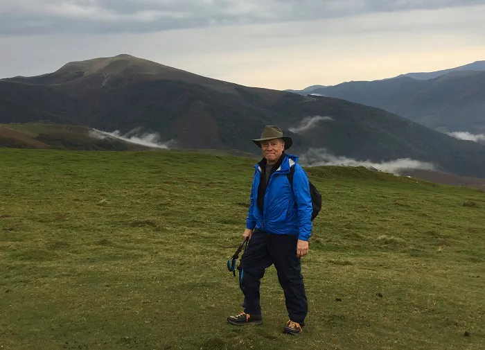 A man standing on a grassy hill in the mountains.