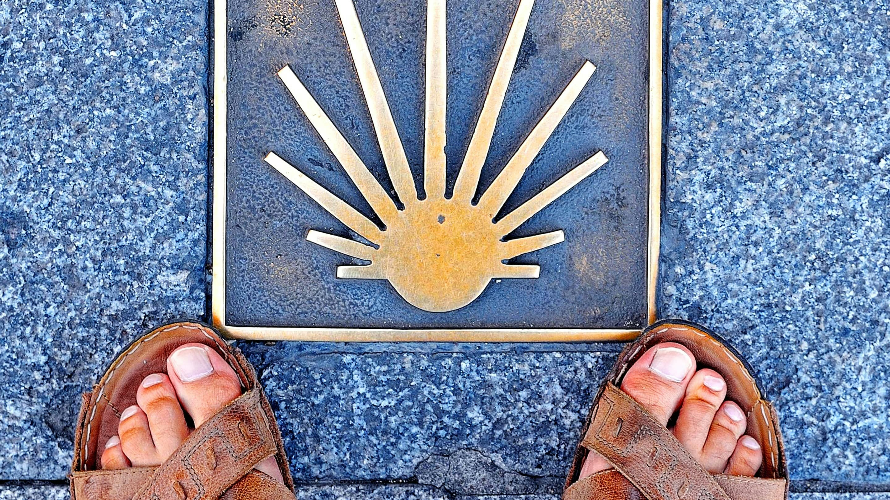A person in sandals standing next to a plaque with a sun on it.