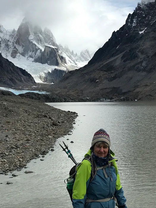 A woman standing in front of a lake with mountains in the background.