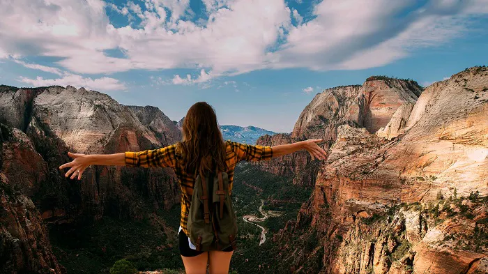 A woman standing on the edge of a canyon with her arms outstretched.