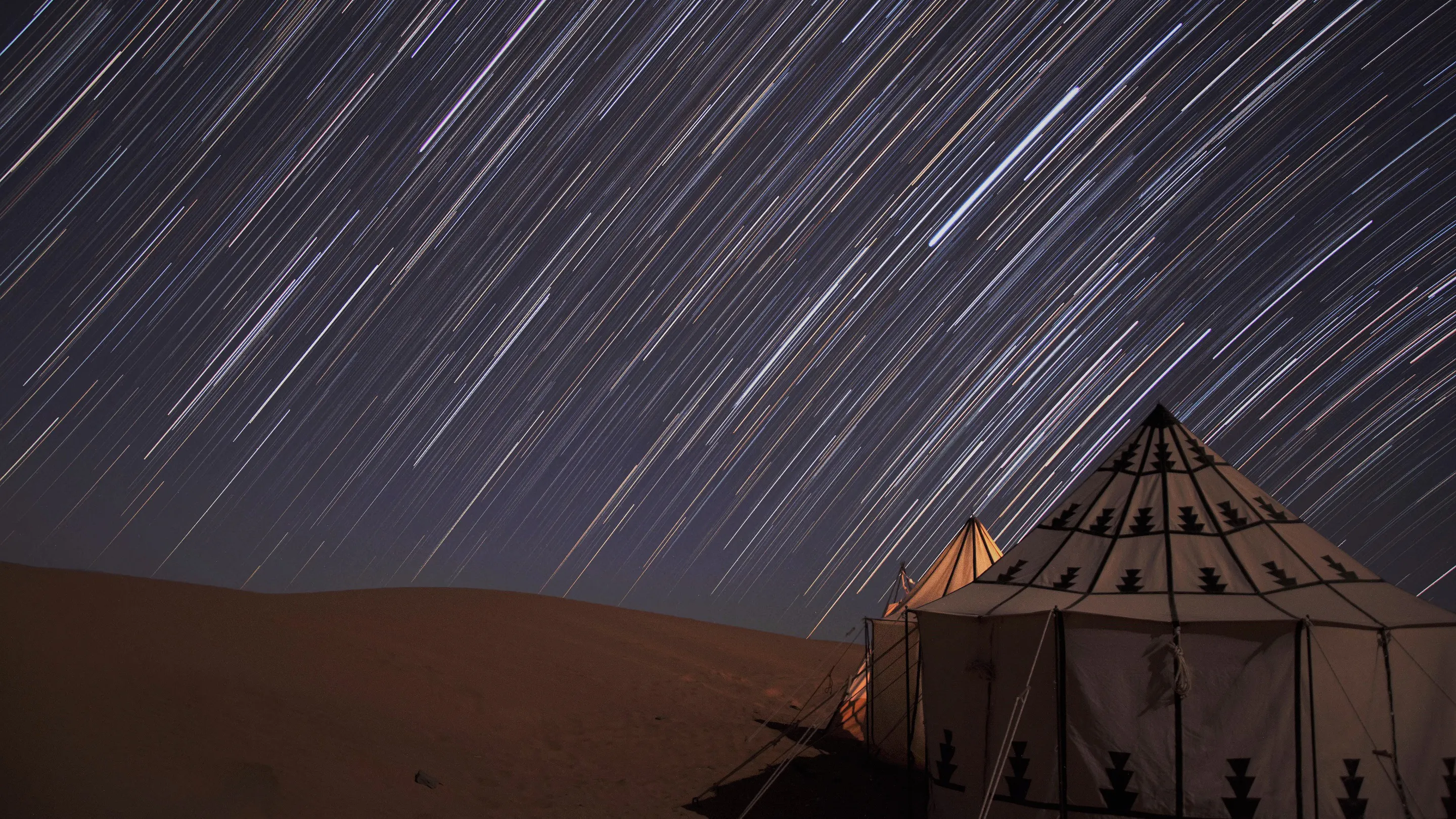 Star trails over a tent in the desert.