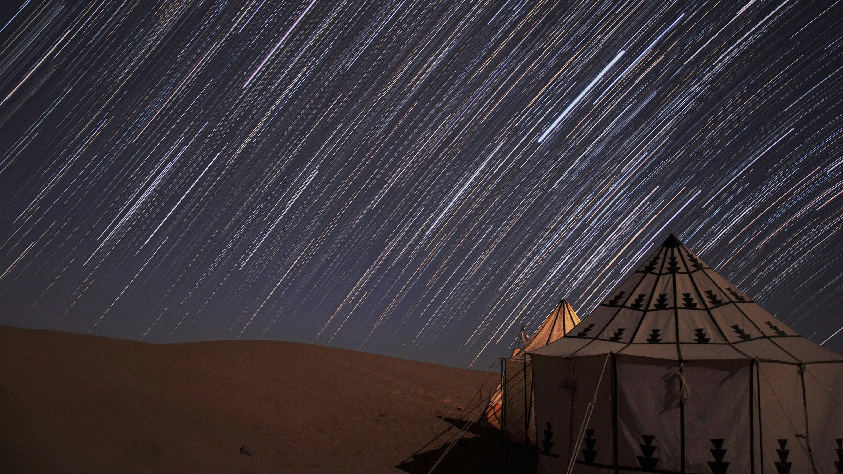 Star trails over a tent in the desert.