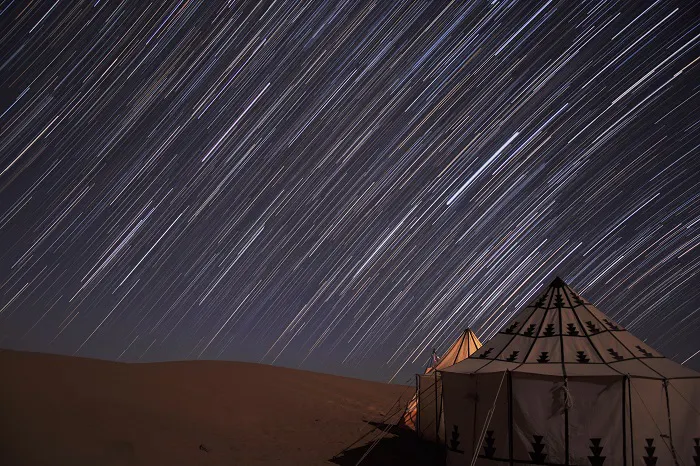 Star trails over a tent in the desert.