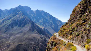 A person is walking down a narrow path in the mountains.