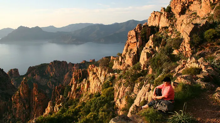 A woman sits on a rocky cliff overlooking the ocean.