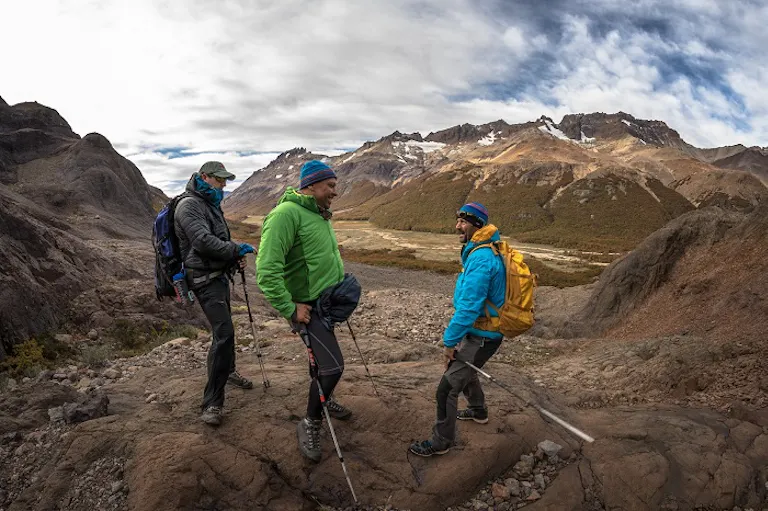group is on a hike break during a hike; each hiker has trekking poles Three hikers on a hiking trip standing on a rocky mountain.