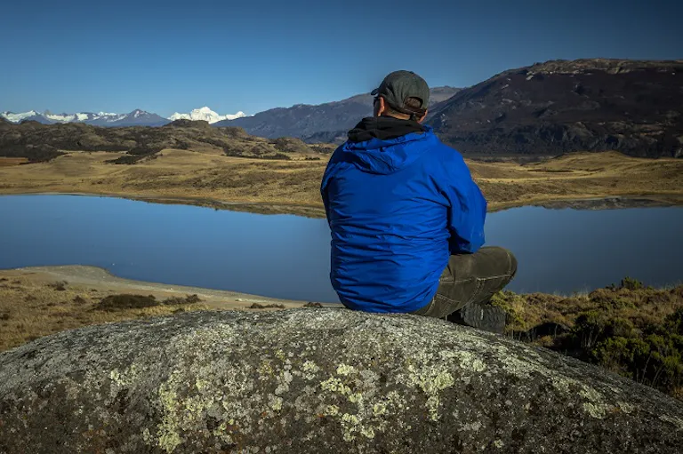 hiking trip with great Patagonia mountain views; man is sitting on a rock next to the water man resting near water trail
