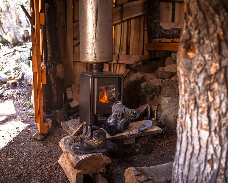 hiking boots and hiking equipment resting on top of wooden logs A wood burning stove in a cabin on a hiking trip.