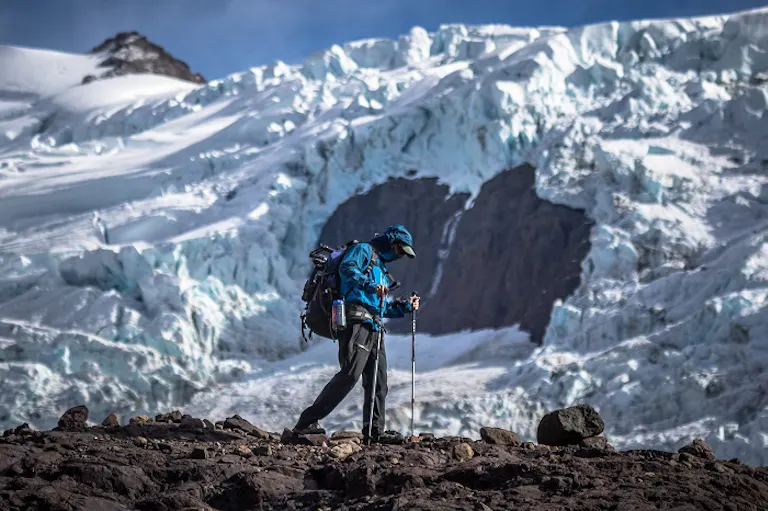 man walks using black solid trekking poles on hiking trip; surrounded by Patagonia mountains A man is hiking on top of a glacier.