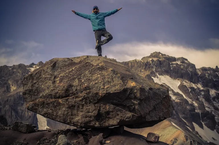 hiking trip in Patagonia; man with blue hiking jacket and beanie A man on a hiking trip standing on top of a rock with his arms outstretched.