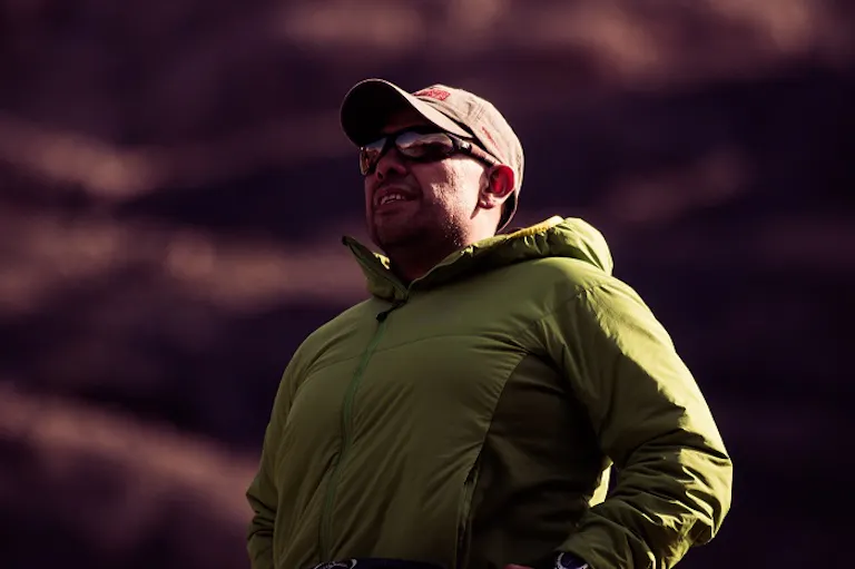 A man on a hiking trip standing on a mountain wearing a green jacket.