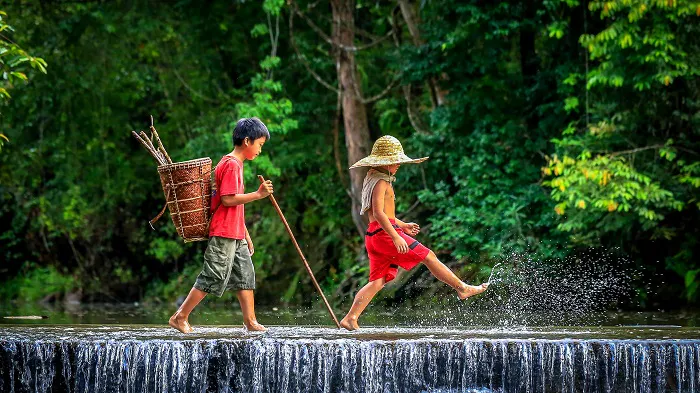 Two boys walking across a waterfall with baskets.