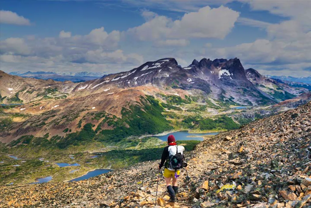 A hiker hiking up a rocky trail with mountains in the background.