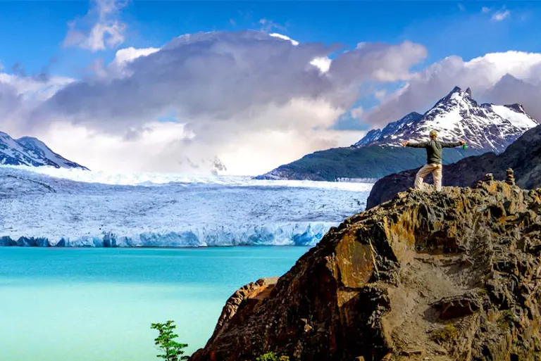 A man standing on top of a rock with a glacier in the background.
