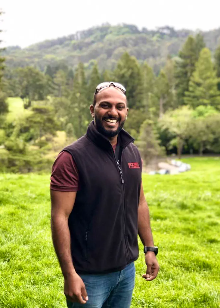 A man in a black vest standing in a grassy field.