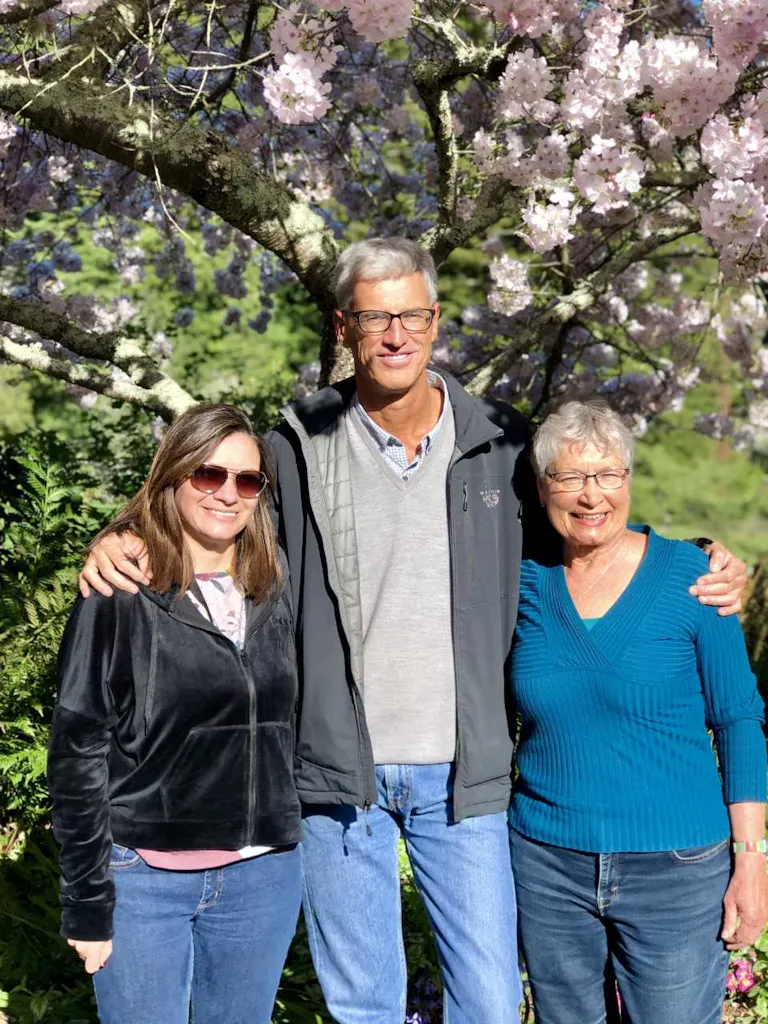 Three people posing in front of a cherry blossom tree.