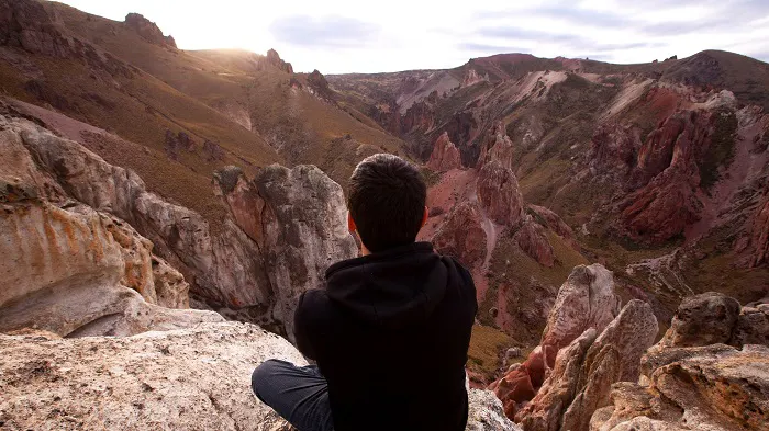 A man sitting on top of a cliff overlooking a canyon.