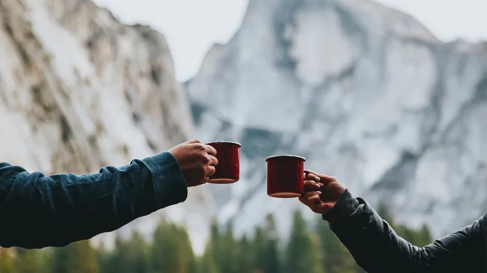 Two people toasting coffee in front of a mountain.