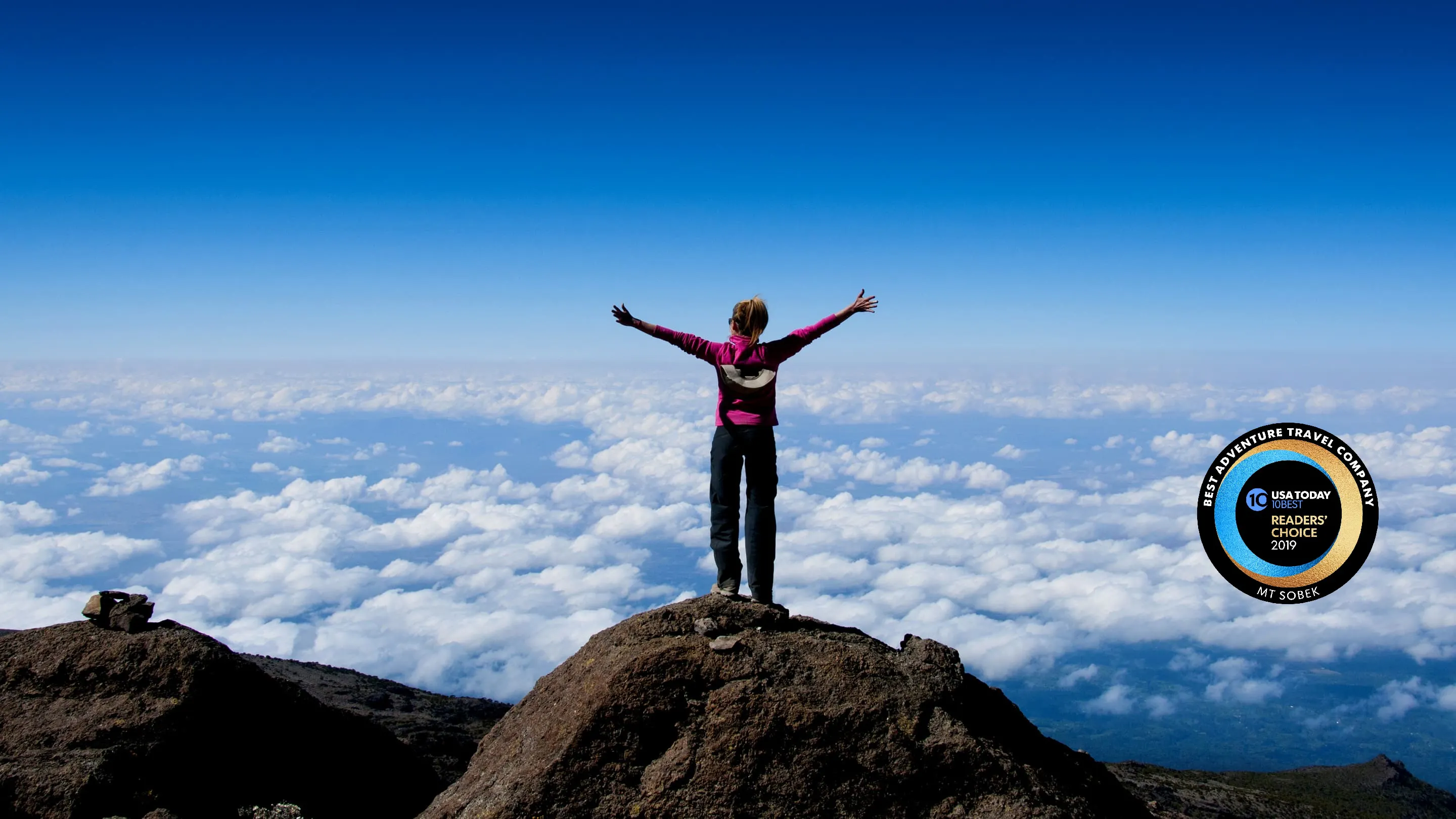 A person standing on top of a mountain with arms outstretched.
