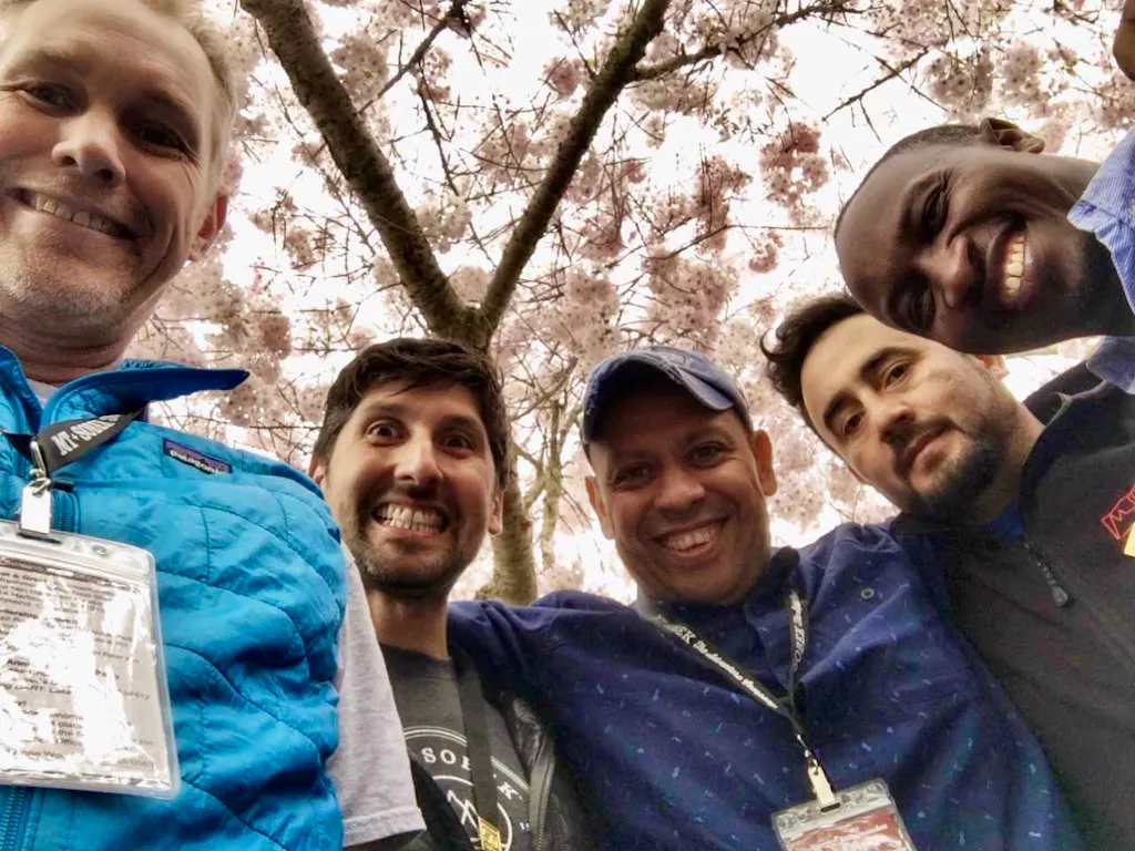 Four men posing for a photo in front of a blossoming cherry tree.