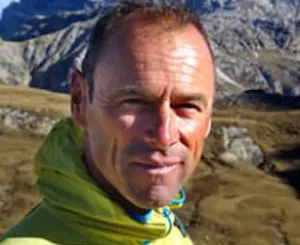 A man in a yellow jacket standing in front of mountains.
