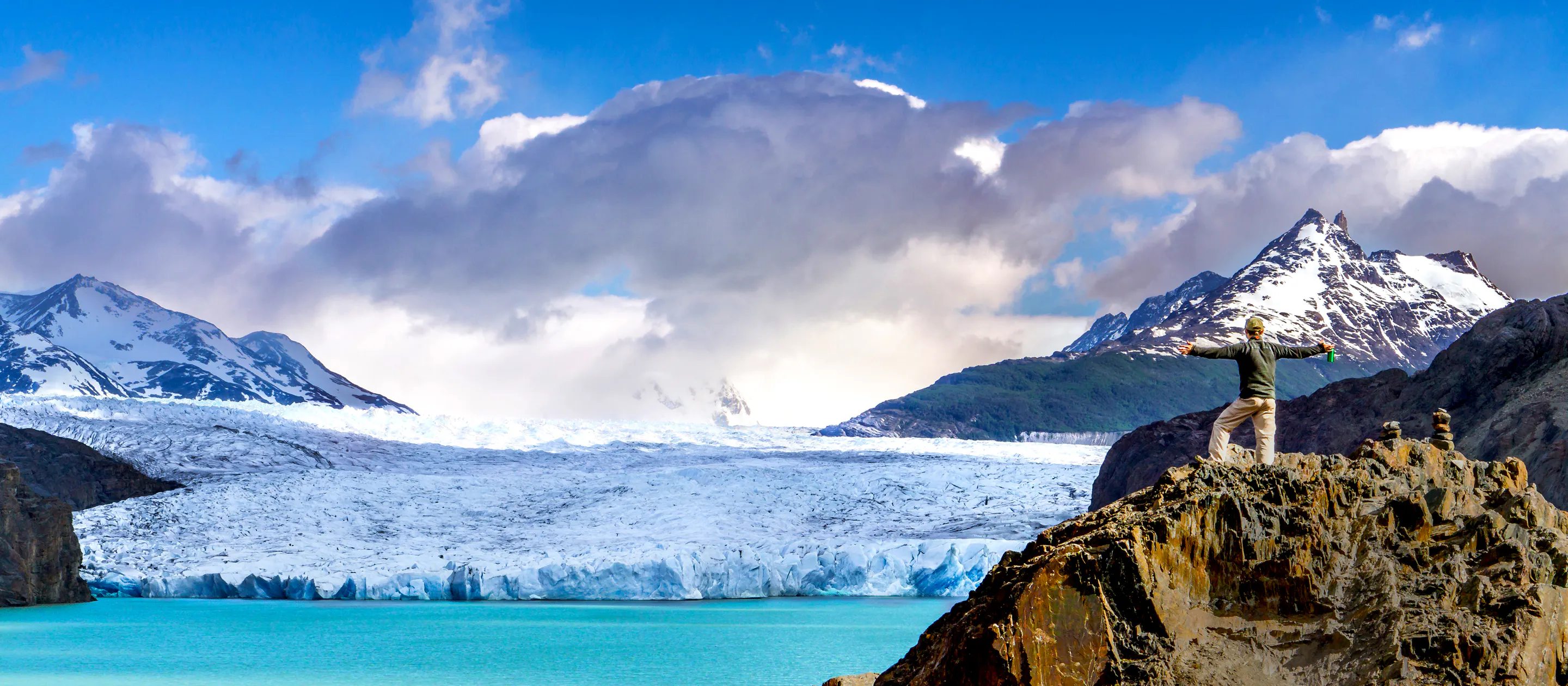 A man standing on top of a rock with a glacier in the background.