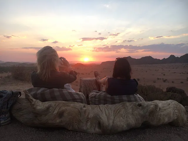 Two women sitting on a couch in the desert watching the sunset.