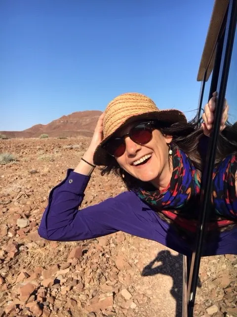 A woman in a hat and sunglasses is taking a selfie in the desert.