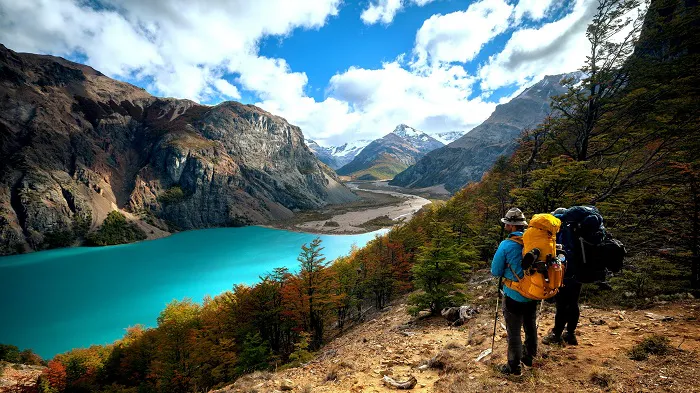 Two hikers looking at a blue lake in the mountains.