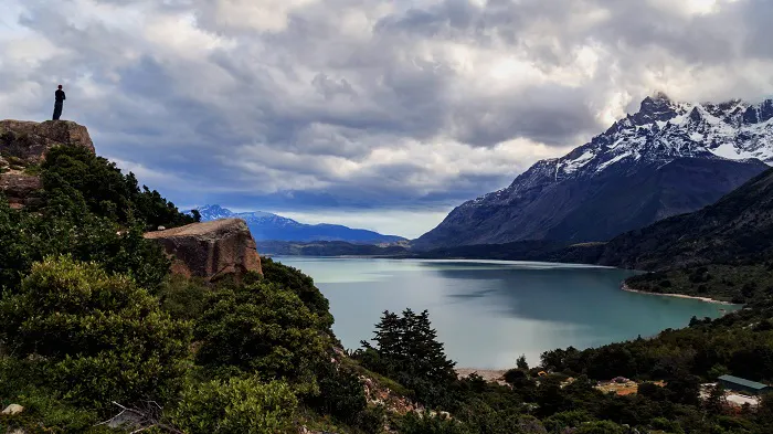 A person standing on top of a mountain overlooking a lake.