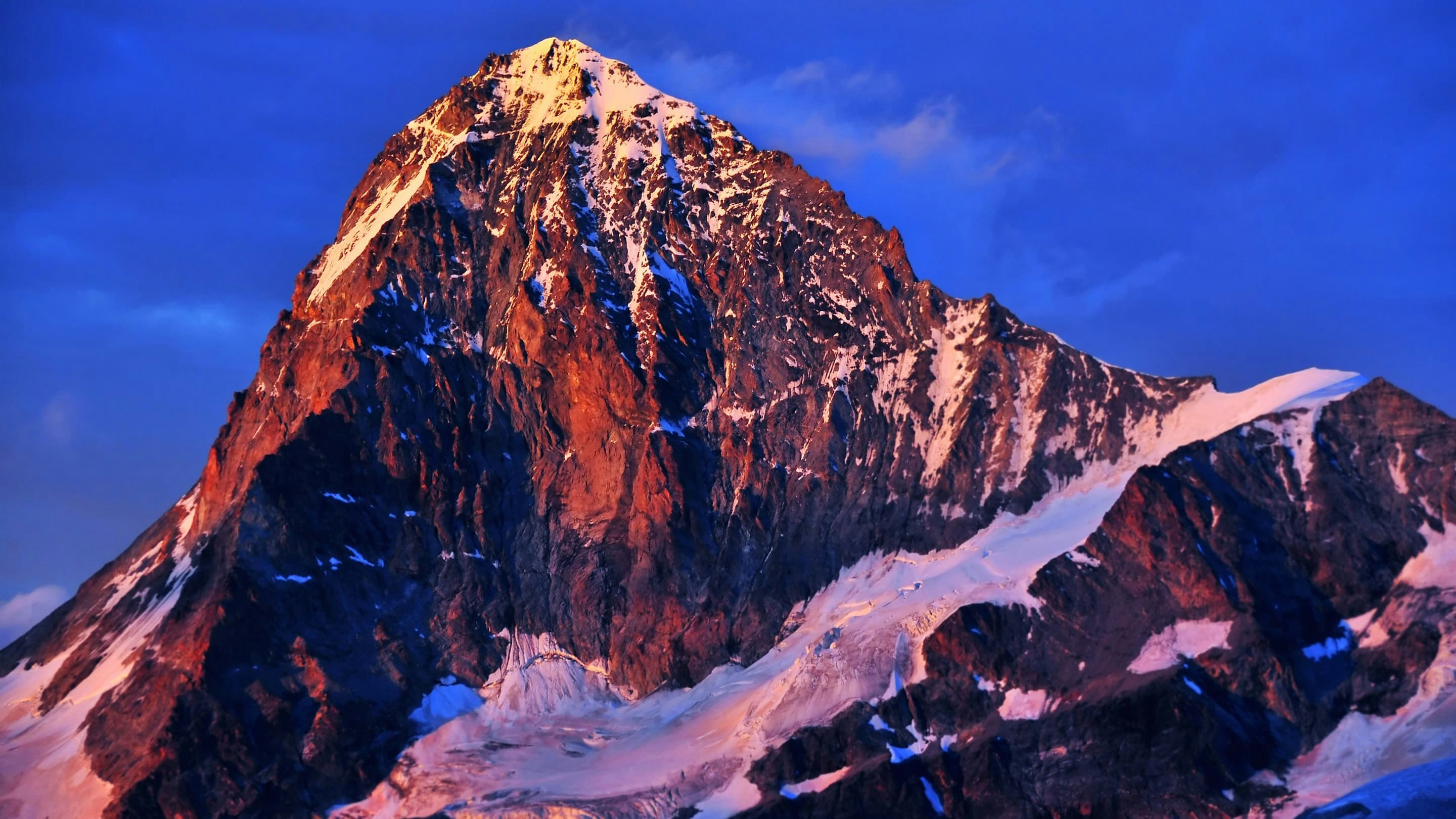 A mountain with snow on it at sunset.
