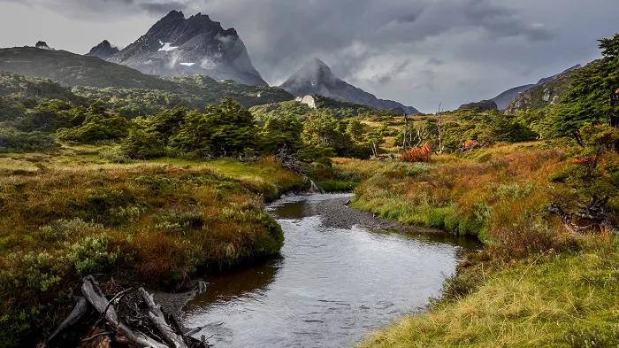 A river runs through a grassy area with mountains in the background.