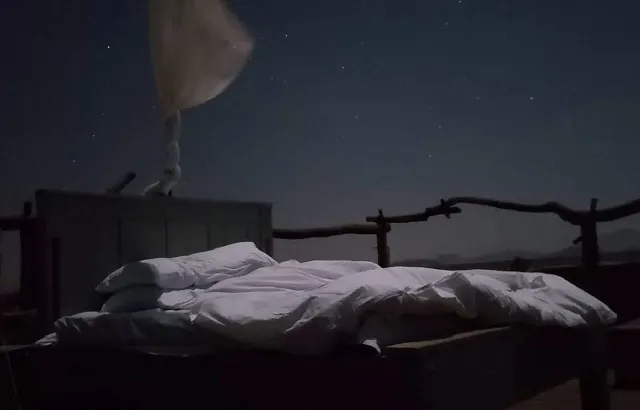 A bed with a white sheet under a starry sky.