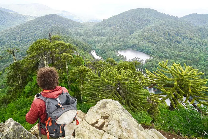 A man with a backpack is standing on top of a mountain overlooking a lake.
