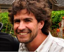 A man with curly hair is smiling next to another man.