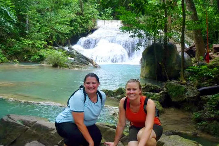 Two women posing in front of a waterfall during their solo travel adventure.